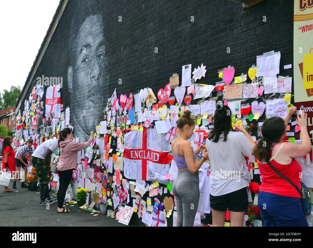 La gente lascia fiori e centinaia di note di supporto, immagini, bandiere e messaggi anti-razzisti sul gigante giocatore britannico di Manchester Marcus Rashford murale a Withington, Manchester, Inghilterra, Regno Unito, che è stato vandalizzato con graffiti abusivi dopo la perdita di calcio in Inghilterra Euro2020 l'11 luglio 2021. Il murale è stato creato dall'artista di strada francese Akse P19 sulla parete del Coffee House Cafe in Copson Street. Marcus Rashford è un calciatore del Manchester United. Akse riparò completamente il murale danneggiato entro il 13 luglio 2021. Data immagine: 13 luglio 2021. Foto Stock