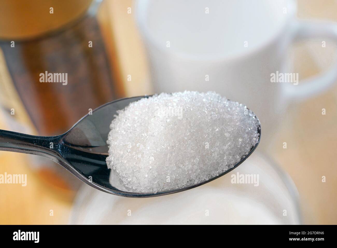 Primo piano di cucchiaio di zucchero. Cucchiaio di zucchero granulato sullo sfondo della tazza bianca e del vasetto di caffè. Concetto di alimentazione malsana. Foto Stock