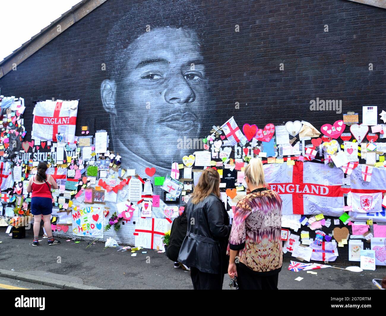 La gente lascia fiori e centinaia di note di supporto, immagini, bandiere e messaggi anti-razzisti sul gigante giocatore britannico di Manchester Marcus Rashford murale a Withington, Manchester, Inghilterra, Regno Unito, che è stato vandalizzato con graffiti abusivi dopo la perdita di calcio in Inghilterra Euro2020 l'11 luglio 2021. Il murale è stato creato dall'artista di strada francese Akse P19 sulla parete del Coffee House Cafe in Copson Street. Marcus Rashford è un calciatore del Manchester United. Akse riparò completamente il murale danneggiato entro il 13 luglio 2021. Data immagine: 13 luglio 2021. Foto Stock