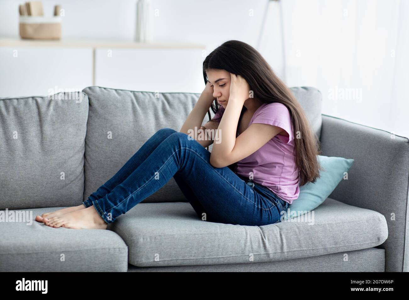 Infelice ragazza teen che tiene la sua testa nella disperazione, sentendosi depresso, seduta sul divano a casa, spazio di copia Foto Stock