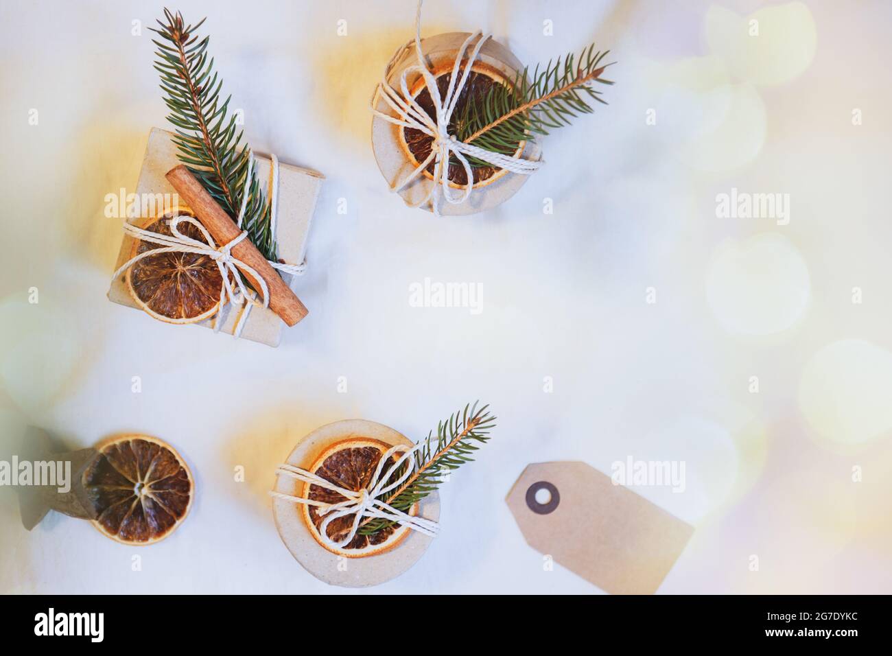 Vista dall'alto scatole regalo di Natale in involucro ecologico decorate con arancio secco naturale, bastone di cannella e ramificazione di abete rosso su sfondo bianco Foto Stock