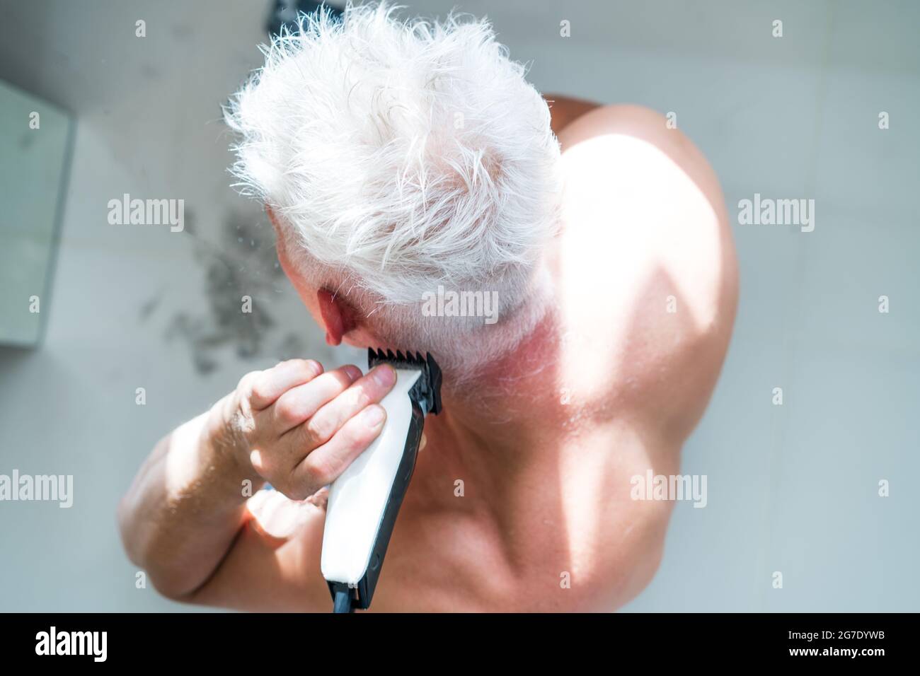 Vista dall'alto l'uomo bianco dei capelli che fa il taglio auto con un regolacapelli e guarda nello specchio. Self-care a casa nelle condizioni di quarantena globale e chiuso Foto Stock