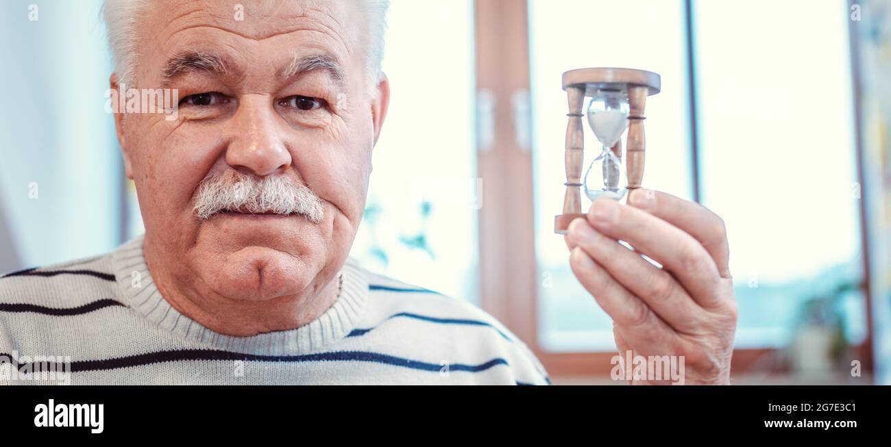 Uomo anziano che tiene clessidra in casa di riposo, simbolo per una durata limitata Foto Stock