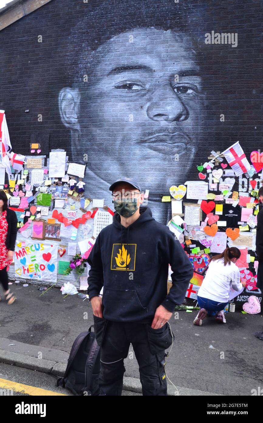 L'artista di strada Akse P19 davanti al murale del gigante Manchester United Marcus Rashford a Withington, Manchester, Inghilterra, Regno Unito, che ha dipinto. Il murale è stato vandalizzato con graffiti abusivi dopo la perdita di calcio in Inghilterra Euro2020 l'11 luglio 2021. Il murale è stato creato dall'artista di strada francese Akse sulla parete del Coffee House Cafe in Copson Street. Marcus Rashford è un calciatore del Manchester United. Akse riparò completamente il murale danneggiato entro il 13 luglio 2021. Data immagine: 13 luglio 2021. Foto Stock