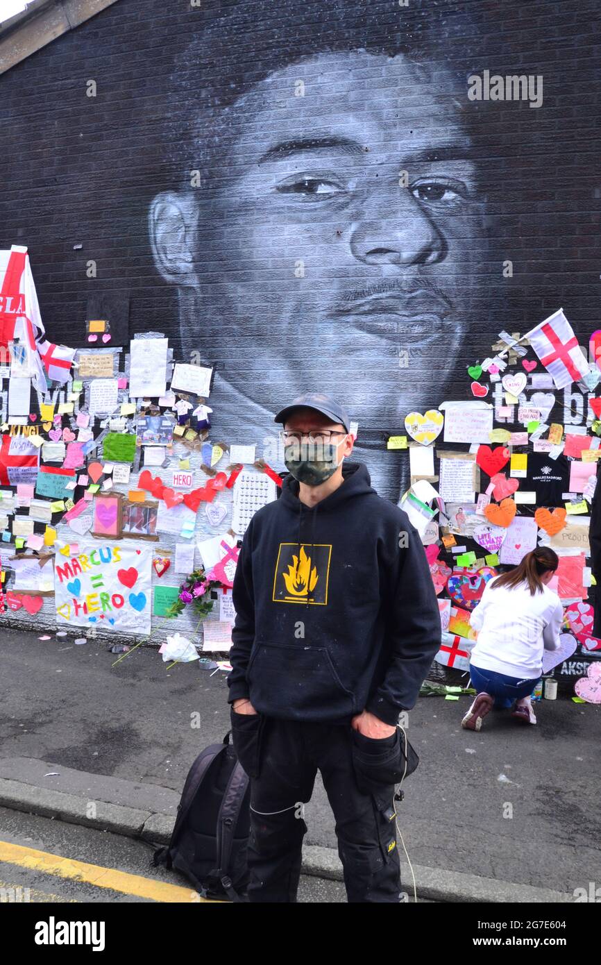 L'artista di strada Akse P19 davanti al murale del gigante Manchester United Marcus Rashford a Withington, Manchester, Inghilterra, Regno Unito, che ha dipinto. Il murale è stato vandalizzato con graffiti abusivi dopo la perdita di calcio in Inghilterra Euro2020 l'11 luglio 2021. Il murale è stato creato dall'artista di strada francese Akse sulla parete del Coffee House Cafe in Copson Street. Marcus Rashford è un calciatore del Manchester United. Akse riparò completamente il murale danneggiato entro il 13 luglio 2021. Data immagine: 13 luglio 2021. Foto Stock