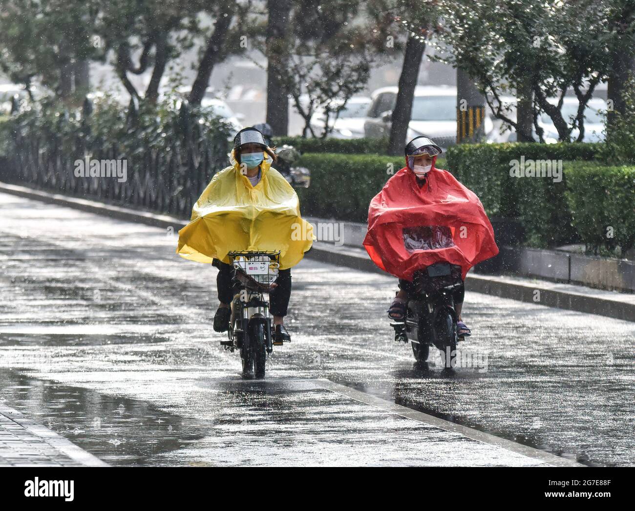 Due uomini che indossano gli impermeabile hanno visto andare in bicicletta  elettrica durante il rainstorm. Lunedì Pechino ha adottato varie misure per  far fronte alla pioggia più pesante che ha colpito la