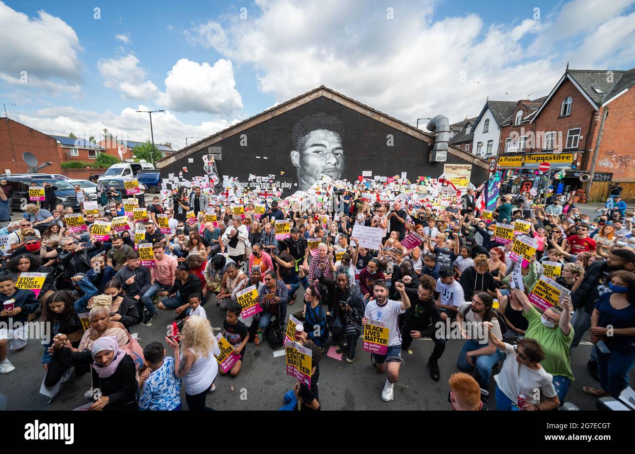 La gente prende il ginocchio durante una dimostrazione a sostegno dello attaccante del Manchester United e del giocatore d'Inghilterra Marcus Rashford davanti al suo murale sul muro del caffè della casa su Copson Street, Withington. Il murale è apparso vandalizzato lunedì dopo che la squadra di calcio inglese ha perso la finale UEFA Euro 2021. Data immagine: Martedì 13 luglio 2021. Il credito fotografico dovrebbe essere: Danny Lawson/PA Wire Foto Stock