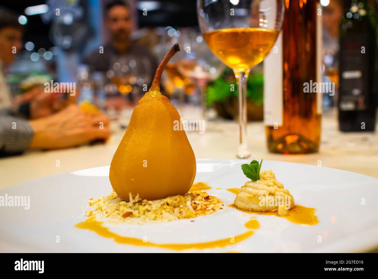 Pera in camicia in vino arancio, farcito con mascarpone e crema di noce, servita con un bicchiere di vino. Delizioso dessert del ristorante. Ristorante e cibi. Foto Stock