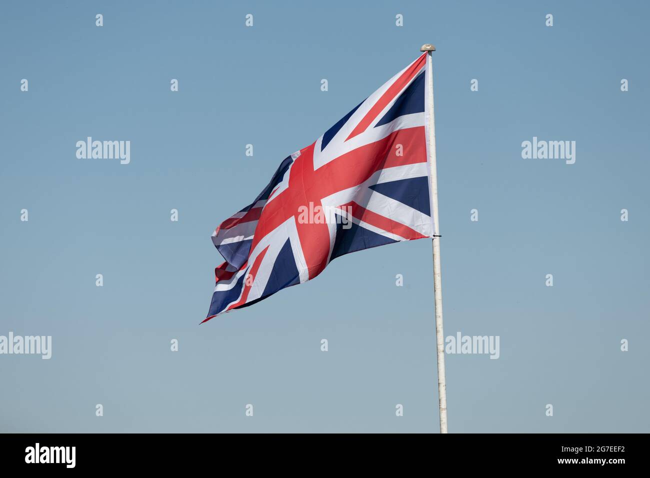 Una fotografia della bandiera di Unione su un albero che soffia delicatamente nel vento. Presa contro un cielo azzurro chiaro Foto Stock