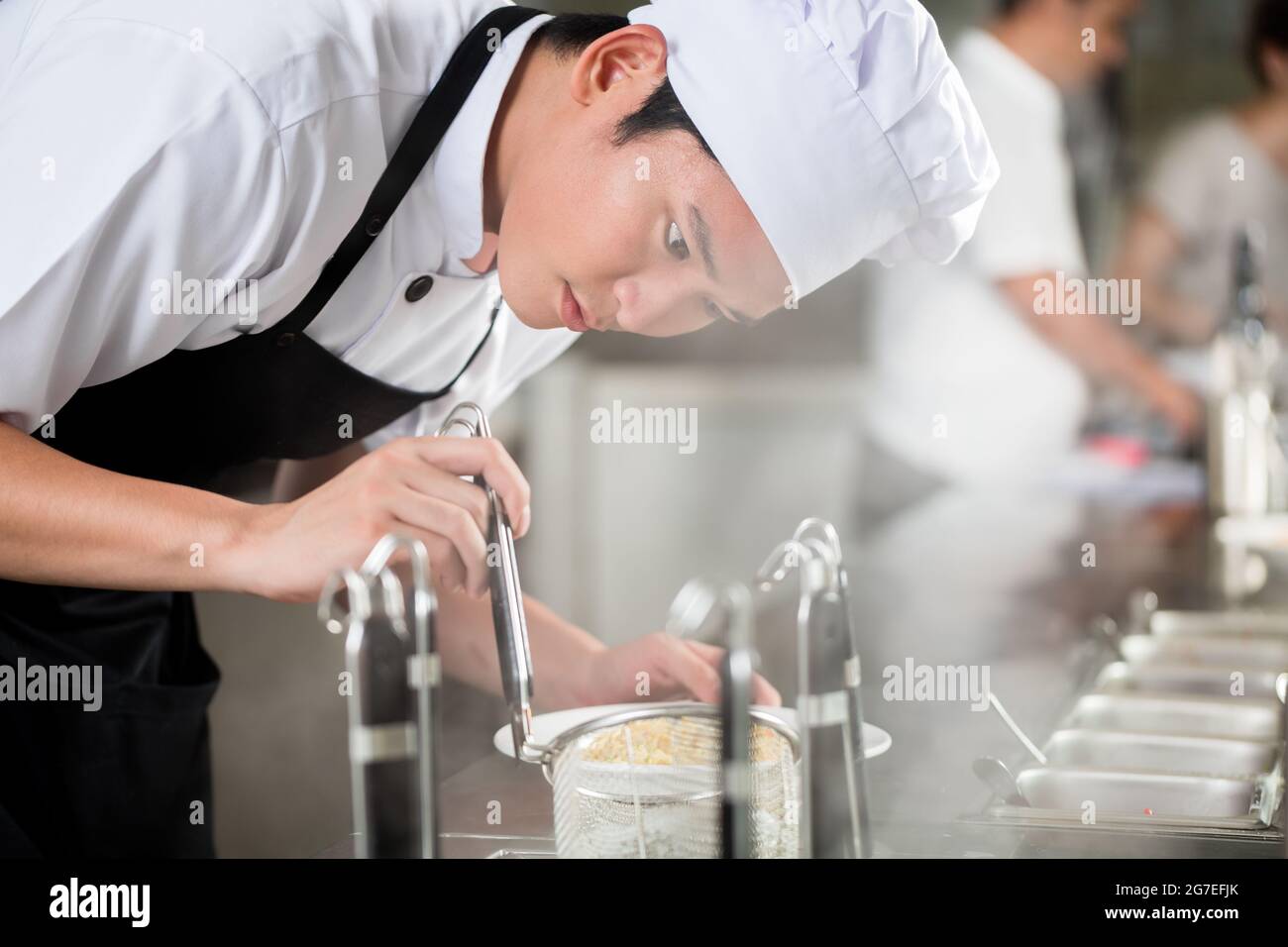 Giovani chef asiatico la placcatura di alimenti in un ristorante con attenzione il pipettaggio guarnire sul lato di una piastra Foto Stock