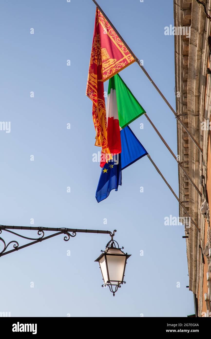 Immagine verticale delle bandiere dell'UE, dell'Italia e di Venezia su un edificio a Venezia Foto Stock