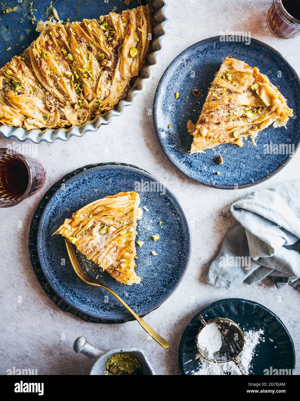 Una torta al latte egiziano di fillo (um Ali) placcata su piatti blu, servita con caffè e guarnire di pistacchio e zucchero di pasticceria Foto Stock
