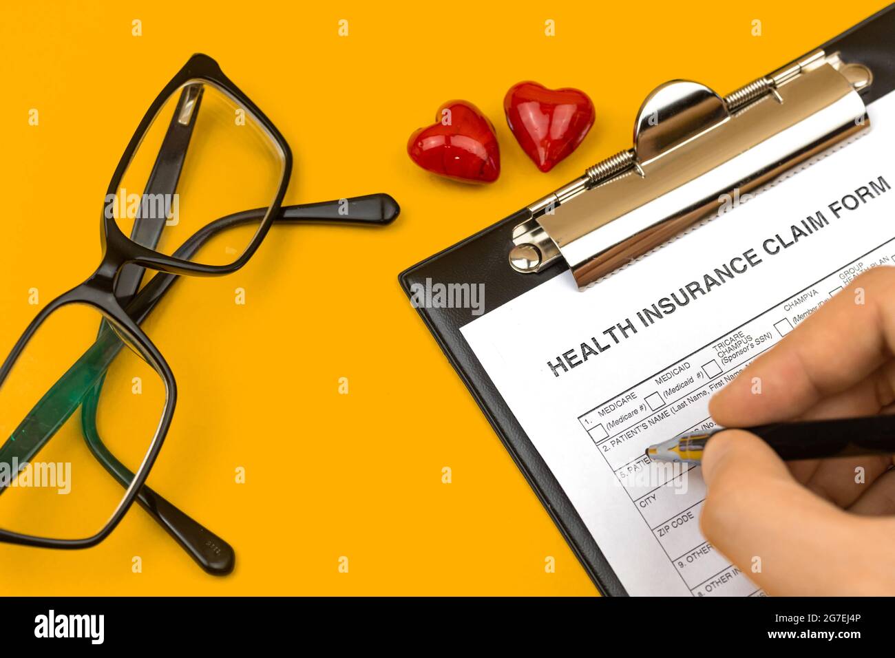Uomo che compila il modulo di richiesta di assicurazione sanitaria. Desktop aziendale con appunti, penna e cuori rossi su un desktop giallo. Vista dall'alto Foto Stock