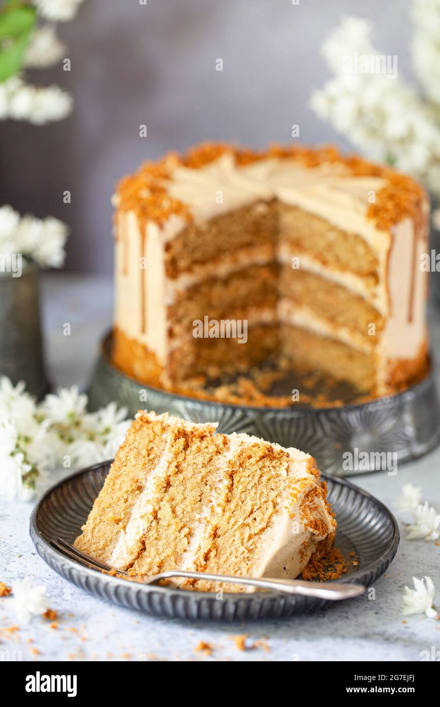 Una fetta di torta al burro con biscotti vegani con biscotti al burro che si gelano davanti all'intera torta Foto Stock