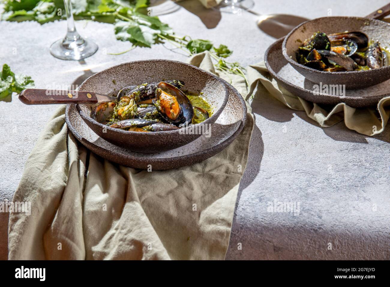 Cena in stile mediterraneo. Primo piano di tavola con cozze in salsa verde e vino bianco. Foto Stock