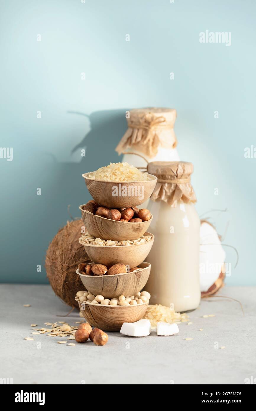 Latte vegano a base di piante non casearie in bottiglie e ingredienti su sfondo blu. Sostituto alternativo del latte senza lattosio Foto Stock