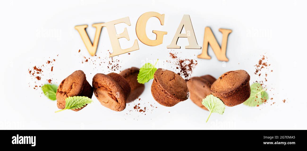 Muffin al cioccolato con foglie di menta su sfondo grigio chiaro, scritte VEGANE realizzate con striscioni di lettere in legno Foto Stock
