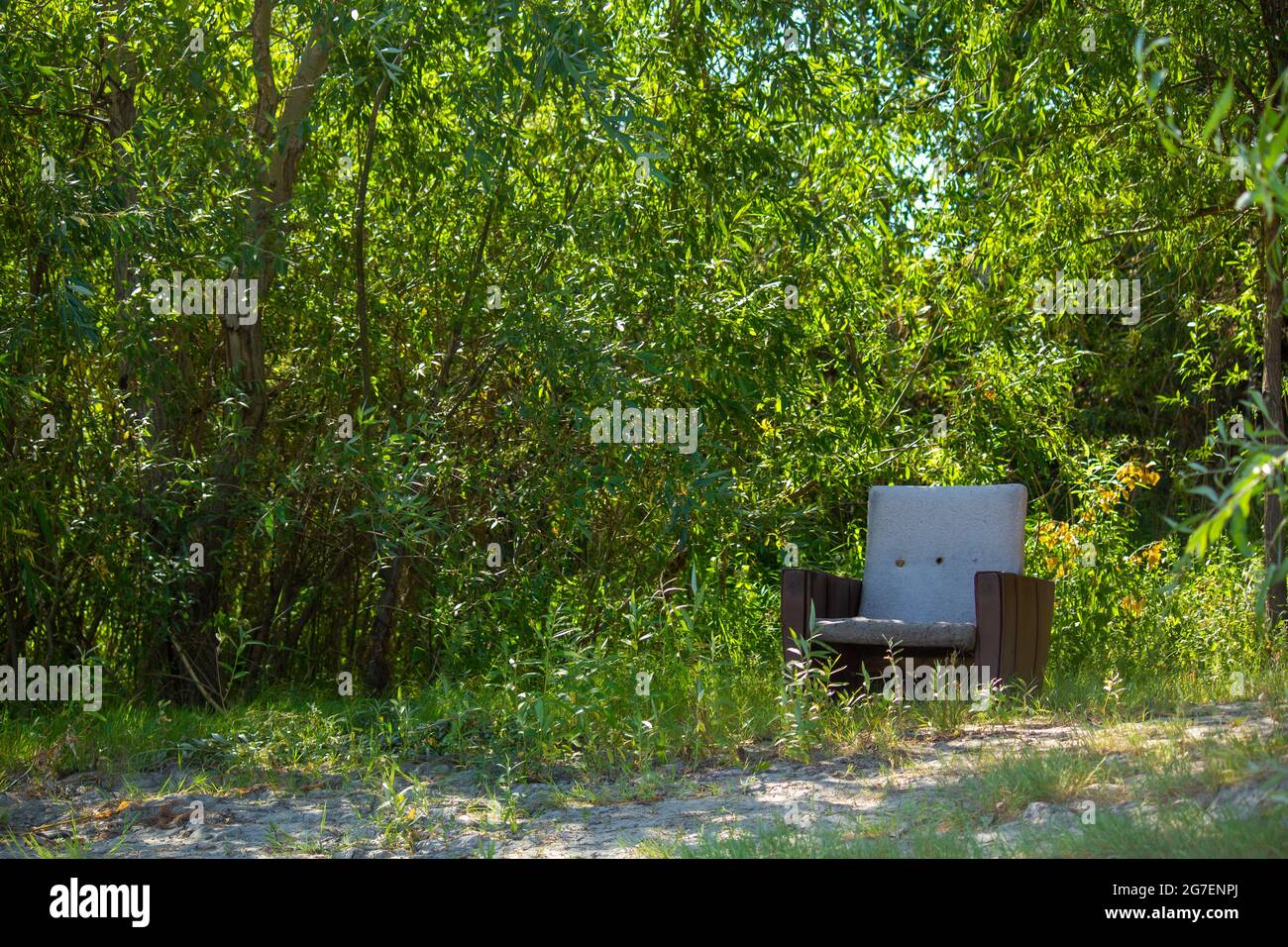 Vecchia sedia all'ombra di alberi sulla riva di un fiume rustico. Concetto di fine settimana e giorni di vacanza in luoghi remoti dalla civiltà in natura. Foto Stock