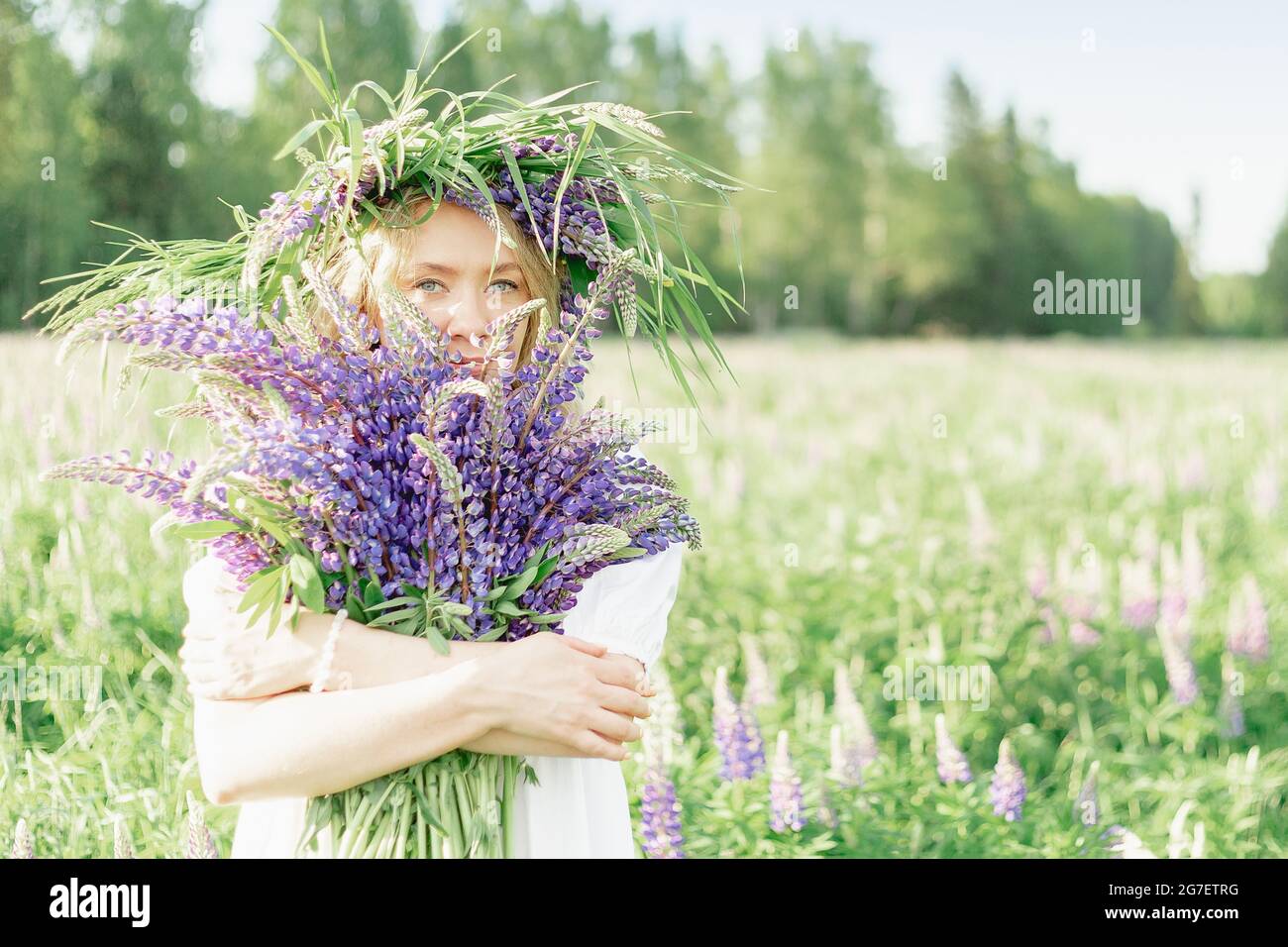 Una ragazza hippy che tiene bouquet di fiori selvatici nelle sue mani. La ragazza nascose il viso dietro un bouquet di lupini. La ragazza tiene il bouquet grande di lupini viola in un Foto Stock