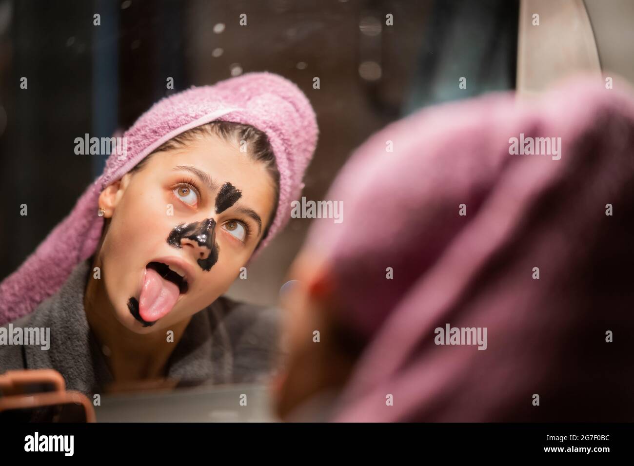 Bella donna con una creta o una maschera di fango sul suo volto mostrando lingua Foto Stock