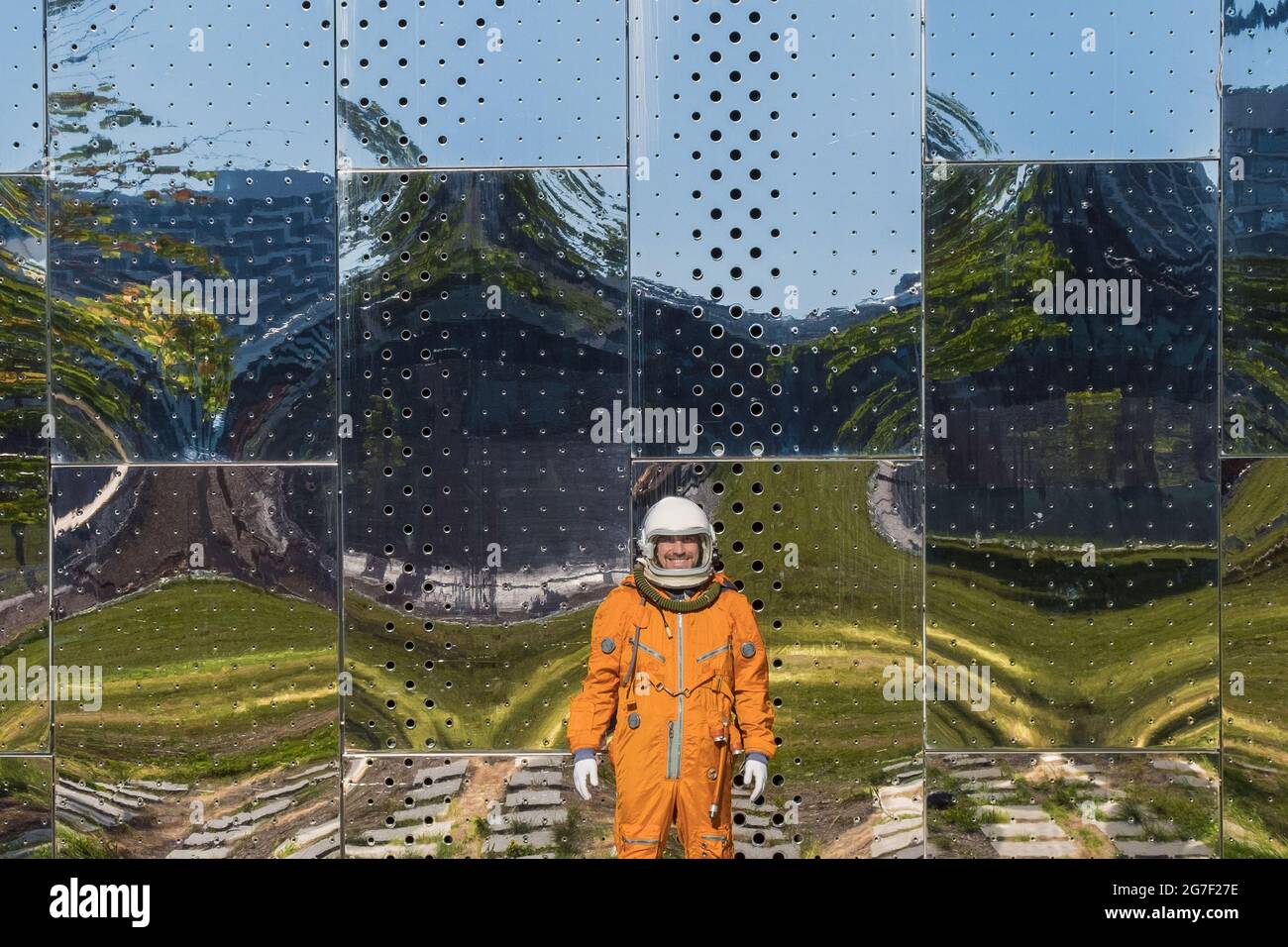 Astronauta che indossa spacesuit arancione e casco spaziale vicino alla parete dello specchio con riflessi Foto Stock