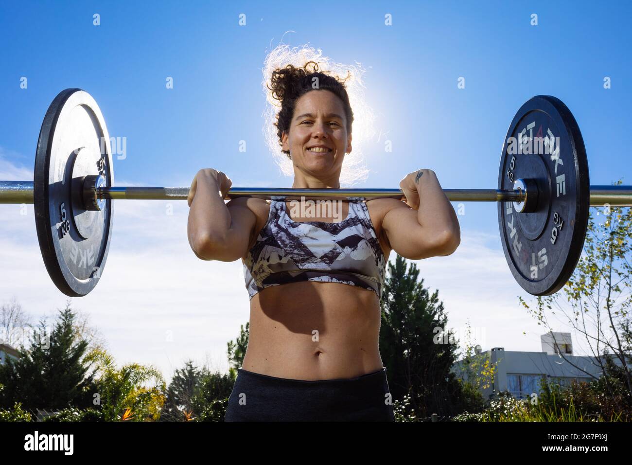 Donna di mezza età che allena crossfit e sollevamento pesi nel suo cortile in posizione pulita e sorridente. Formato orizzontale. Foto Stock