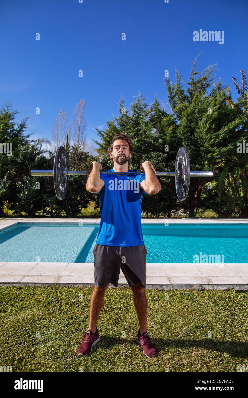 Uomo di mezza età che si adopera su crossfit e sollevamento pesi nel suo cortile Foto Stock