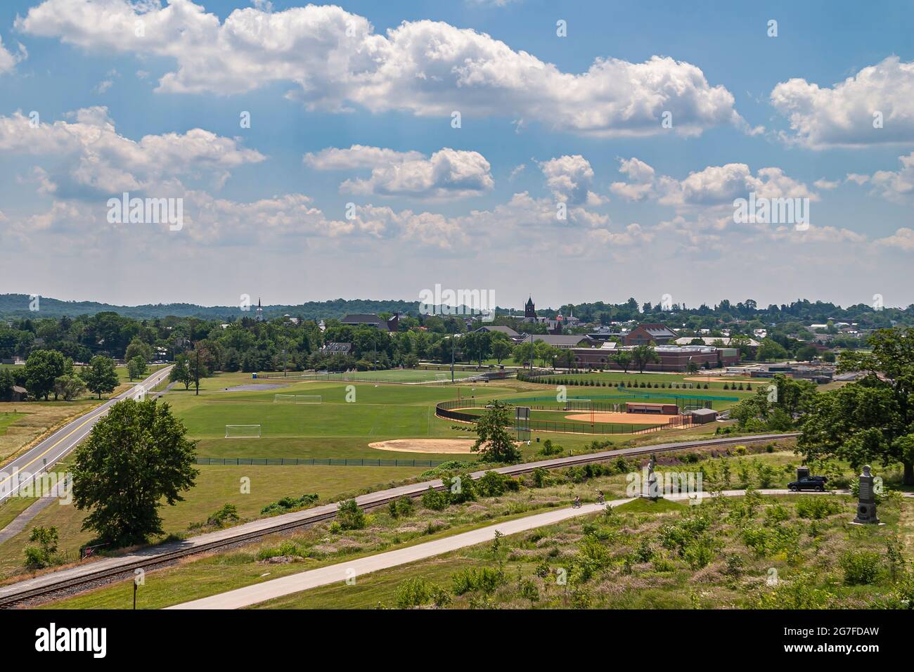 Gettysburg, PA, USA - 15 giugno 2008: Gli edifici universitari locali dietro il terreno sportivo verde West Field sotto il paesaggio blu del cielo. Centro città con chiesa sp Foto Stock