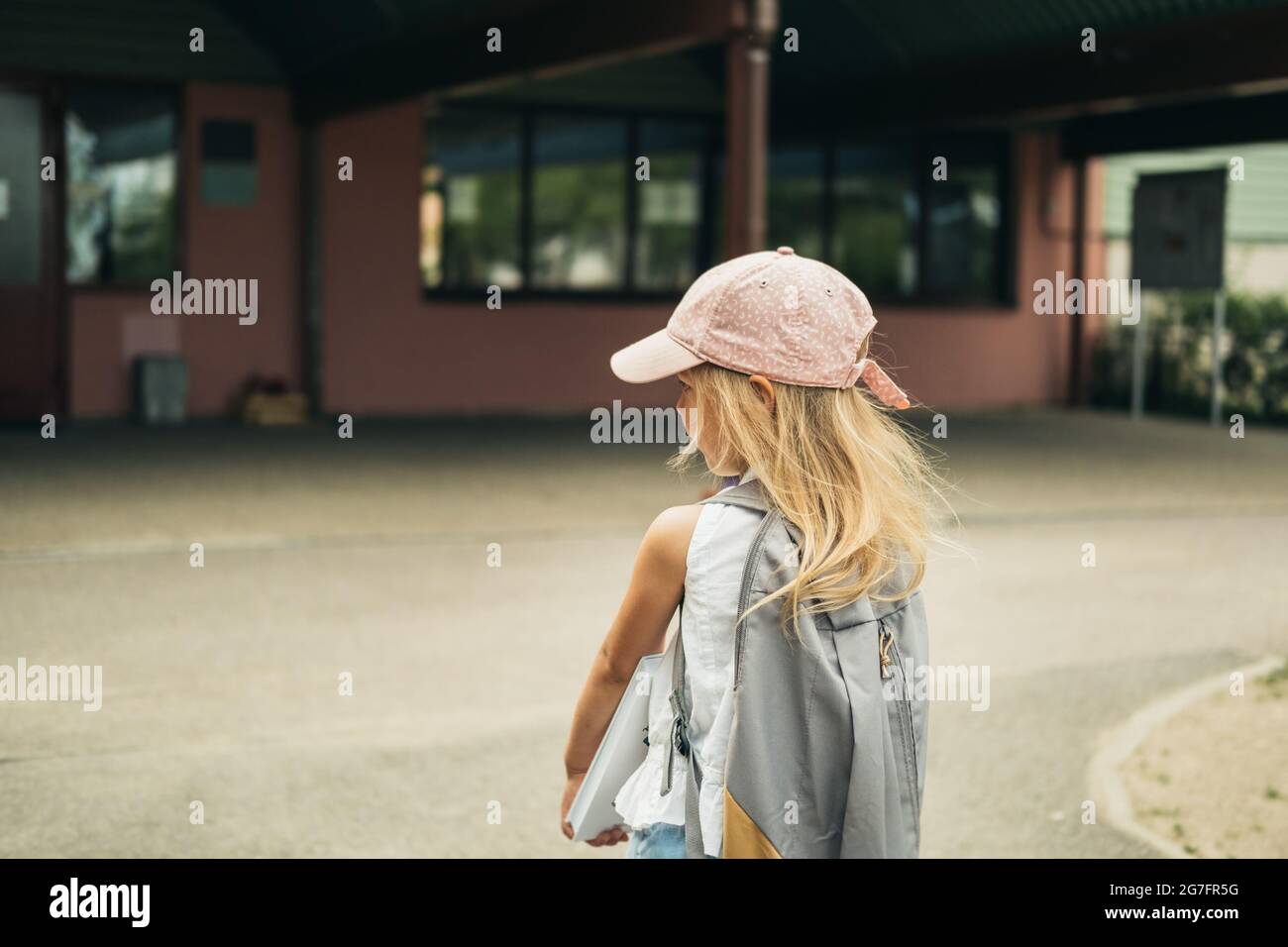 La ragazza carina, studente di scuola elementare, a piedi a scuola con borsa dietro e libro. Gli studenti sono pronti per il nuovo anno. Ritorno a scuola. Foto Stock