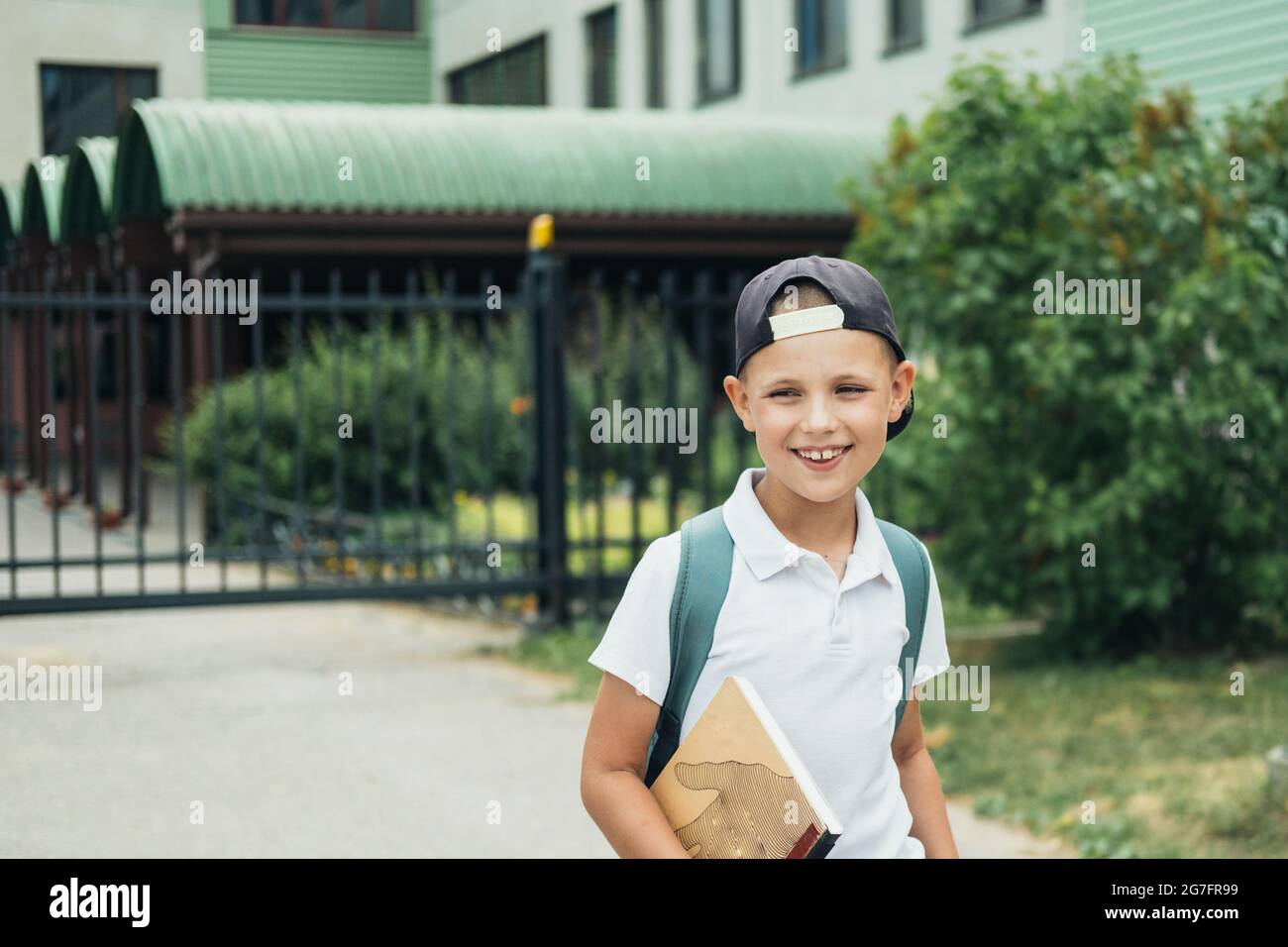 Ragazzo sorridente, studente di scuola elementare, a piedi a scuola con borsa dietro e libro. Gli studenti sono pronti per il nuovo anno. Ritorno a scuola. Foto Stock