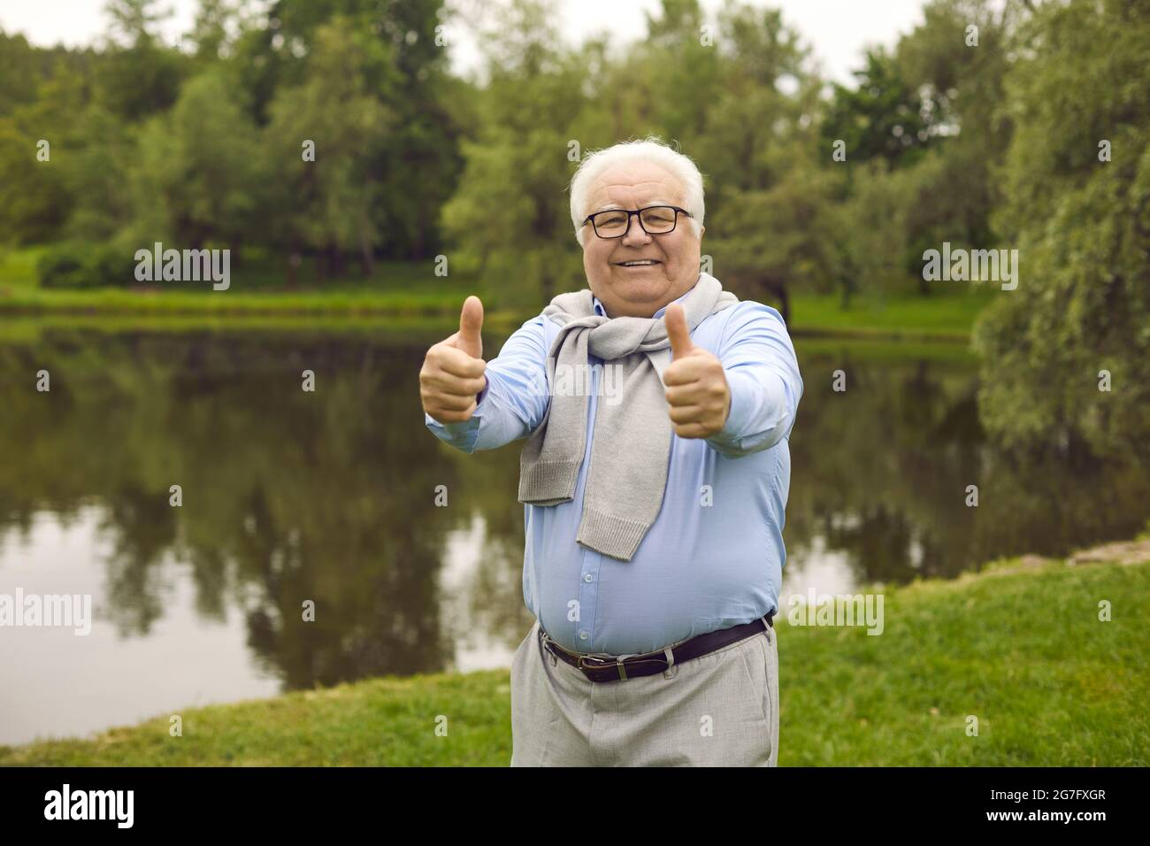 Ritratto di un felice anziano in piedi in un parco verde e dando un pollice in su Foto Stock