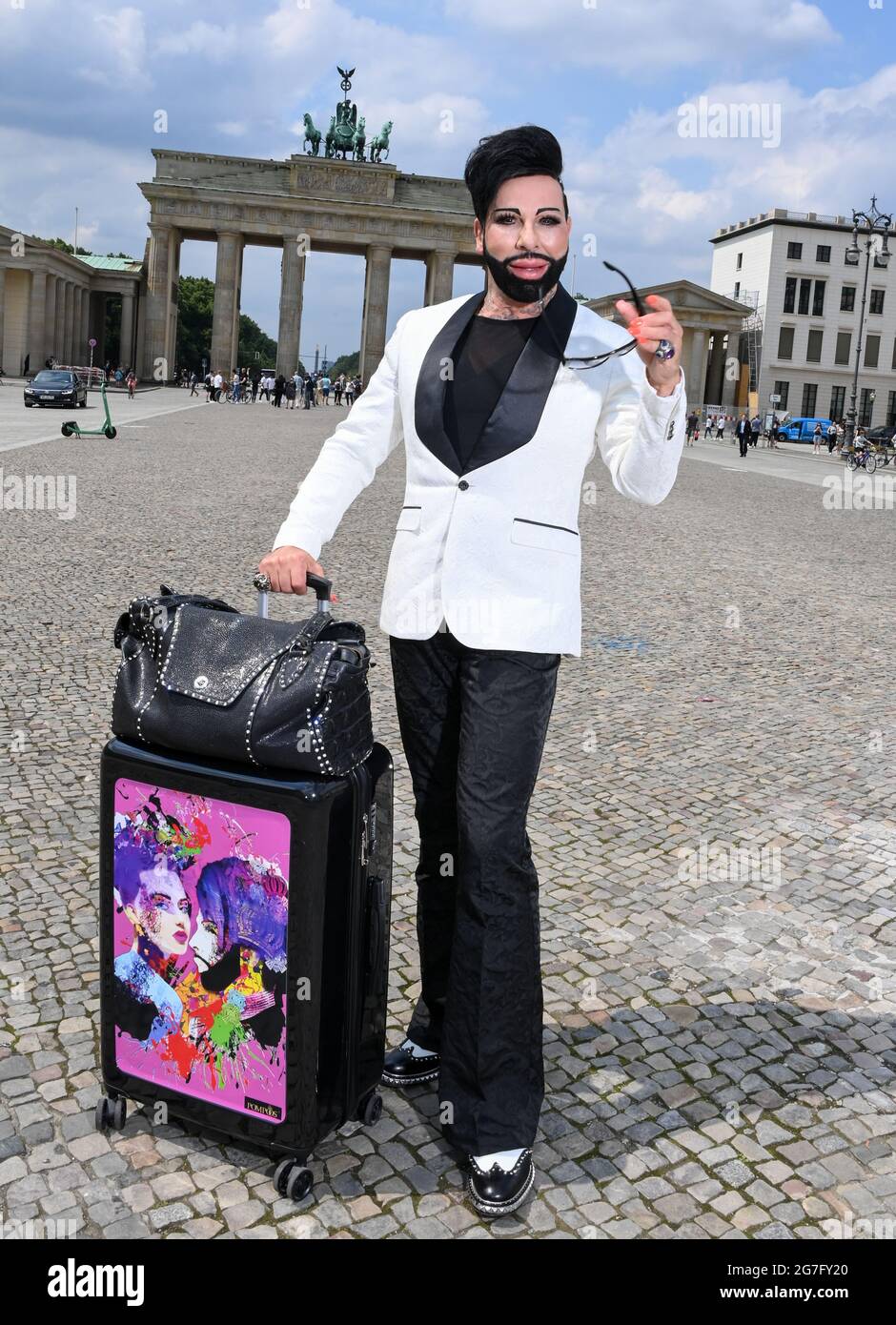 Berlino, Germania. 12 luglio 2021. Lo stilista Harald Glööckler, qui con  una valigia davanti alla porta di Brandeburgo, vuole tornare più spesso  nella capitale tedesca in futuro, sei anni dopo il trasferimento