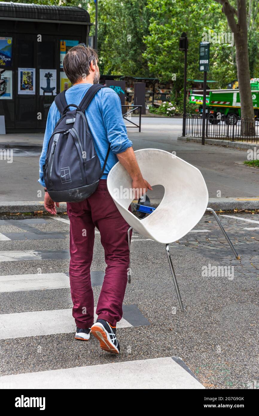 Giovane uomo che attraversa la strada con una sedia moderna - Parigi, Francia. Foto Stock