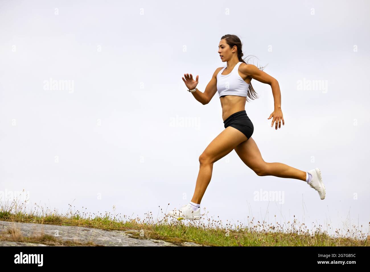 Atleta femminile determinata Fit che corre su montagna contro cielo Foto Stock