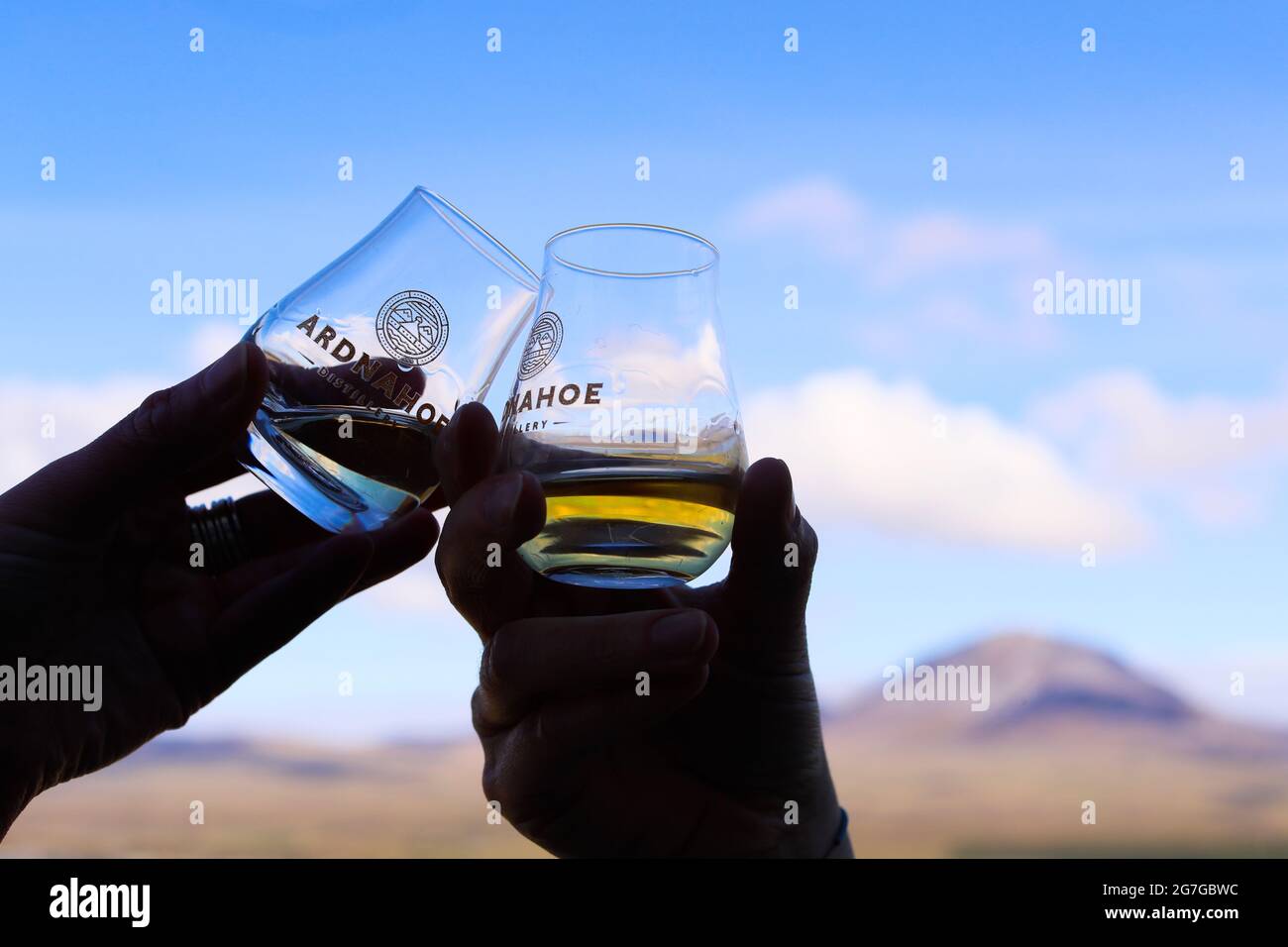 Bere whisky alla distilleria Ardnahoe sull'isola di Islay della costa occidentale della Scozia con i Paps del Giura all'orizzonte. Foto Stock