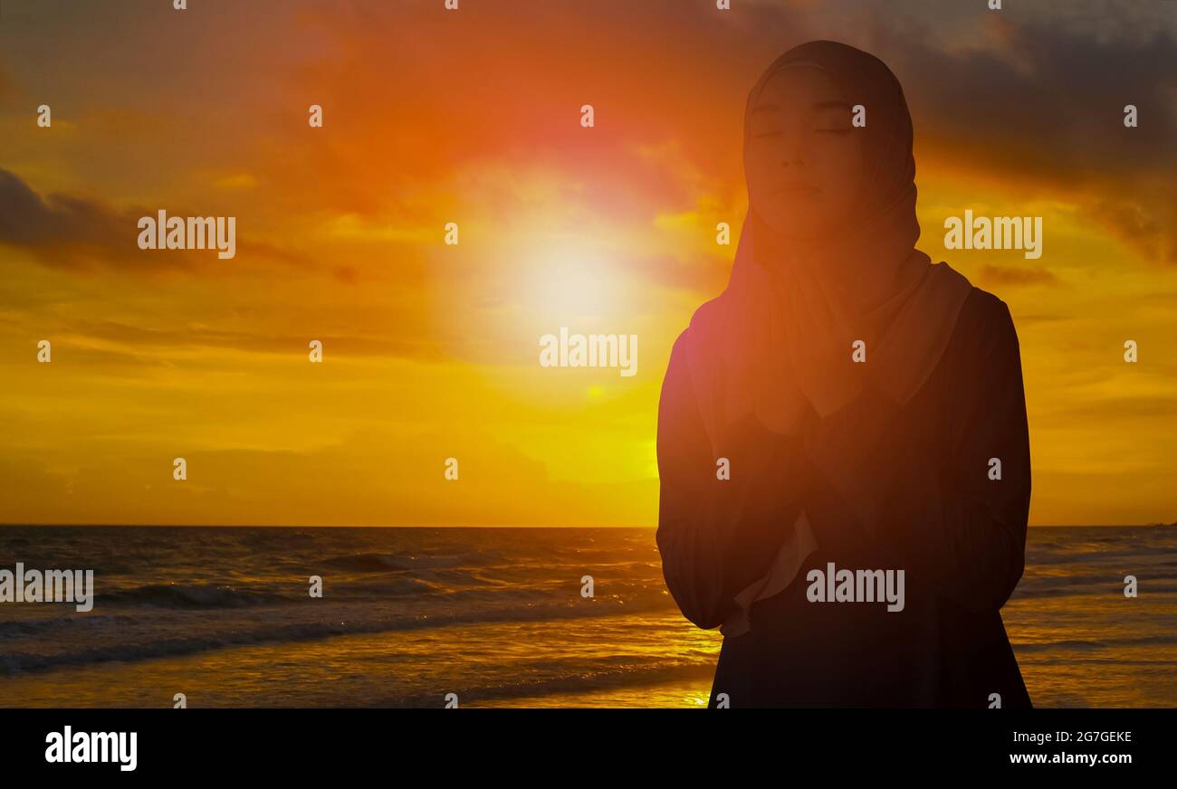 Silhouette di giovane donna musulmana in un hijab nero, in piedi con la sua schiena al tramonto, rituale religioso concetto per la pace e la tranquillità. Foto Stock