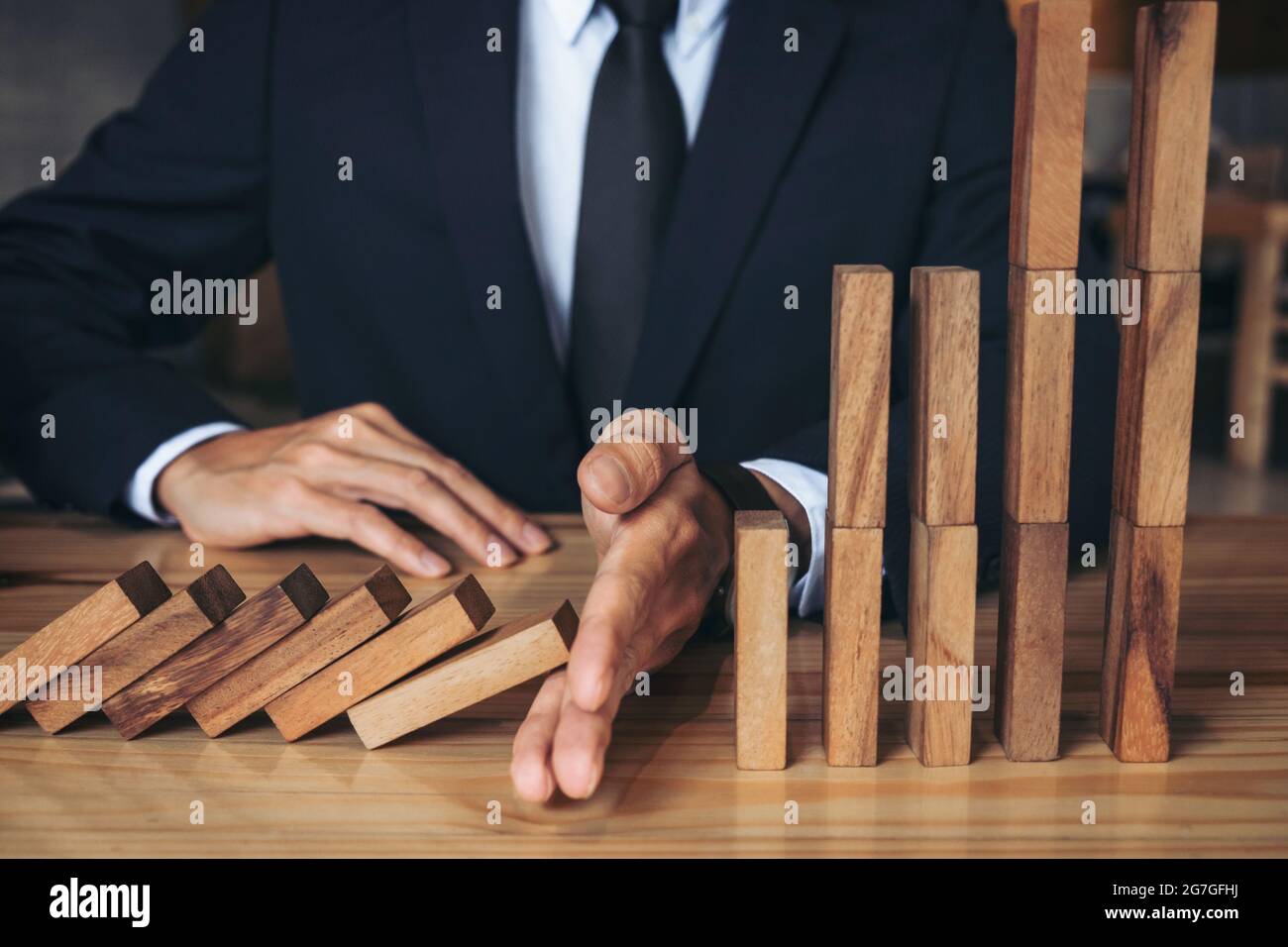 Primo piano di uomo d'affari mano arresto caduta Dominoes effetto di legno da continuo rovesciato o rischio, strategia e concetto di intervento di successo per Foto Stock