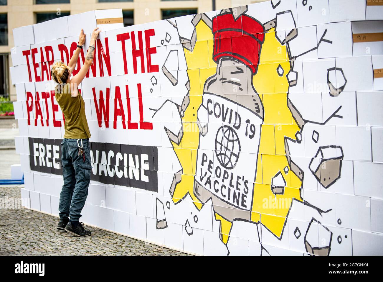 Berlino, Germania. 14 luglio 2021. Un attivista crea un simbolico "muro di brevetto" di fronte alla porta di Brandeburgo. Gli attivisti di Avaaz chiedono la sospensione temporanea della protezione brevettuale per i vaccini Covid. Credit: Fabian Sommer/dpa/Alamy Live News Foto Stock