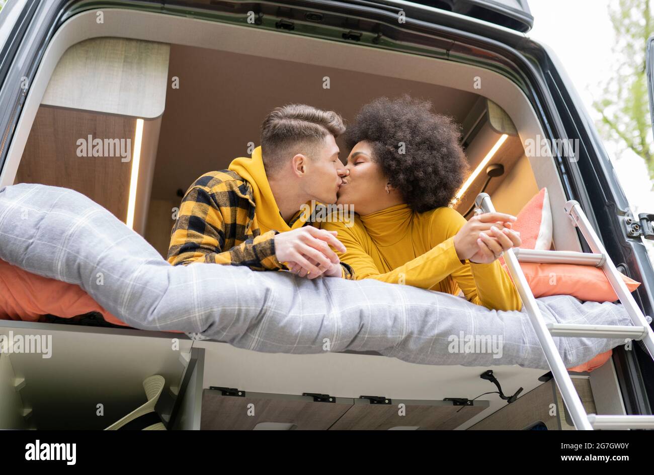 Vista laterale di diversi uomini e donne baciarsi mentre sdraiati sul letto in un pulmino moderno durante il viaggio Foto Stock
