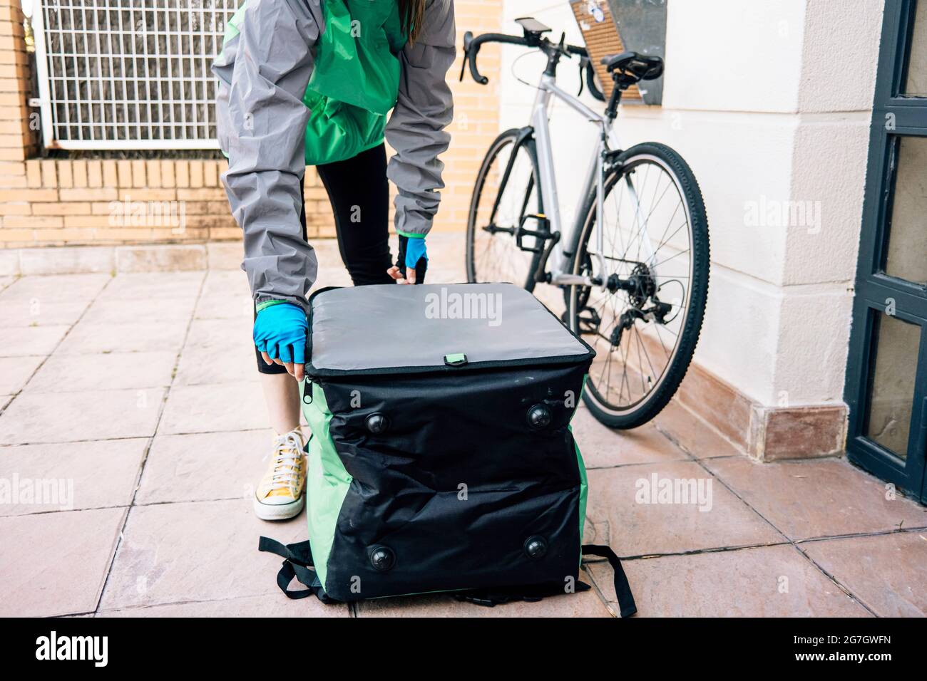 Corriere femminile anonimo in sacchetto termico isolato ad apertura uniforme su pavimento piastrellato vicino alla porta durante la consegna Foto Stock