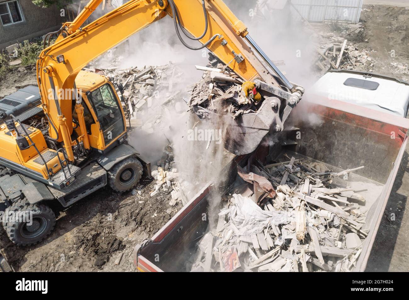L'escavatore carica i detriti di costruzione del vecchio edificio dopo la distruzione nel dumper, vista aerea dal drone. Foto Stock