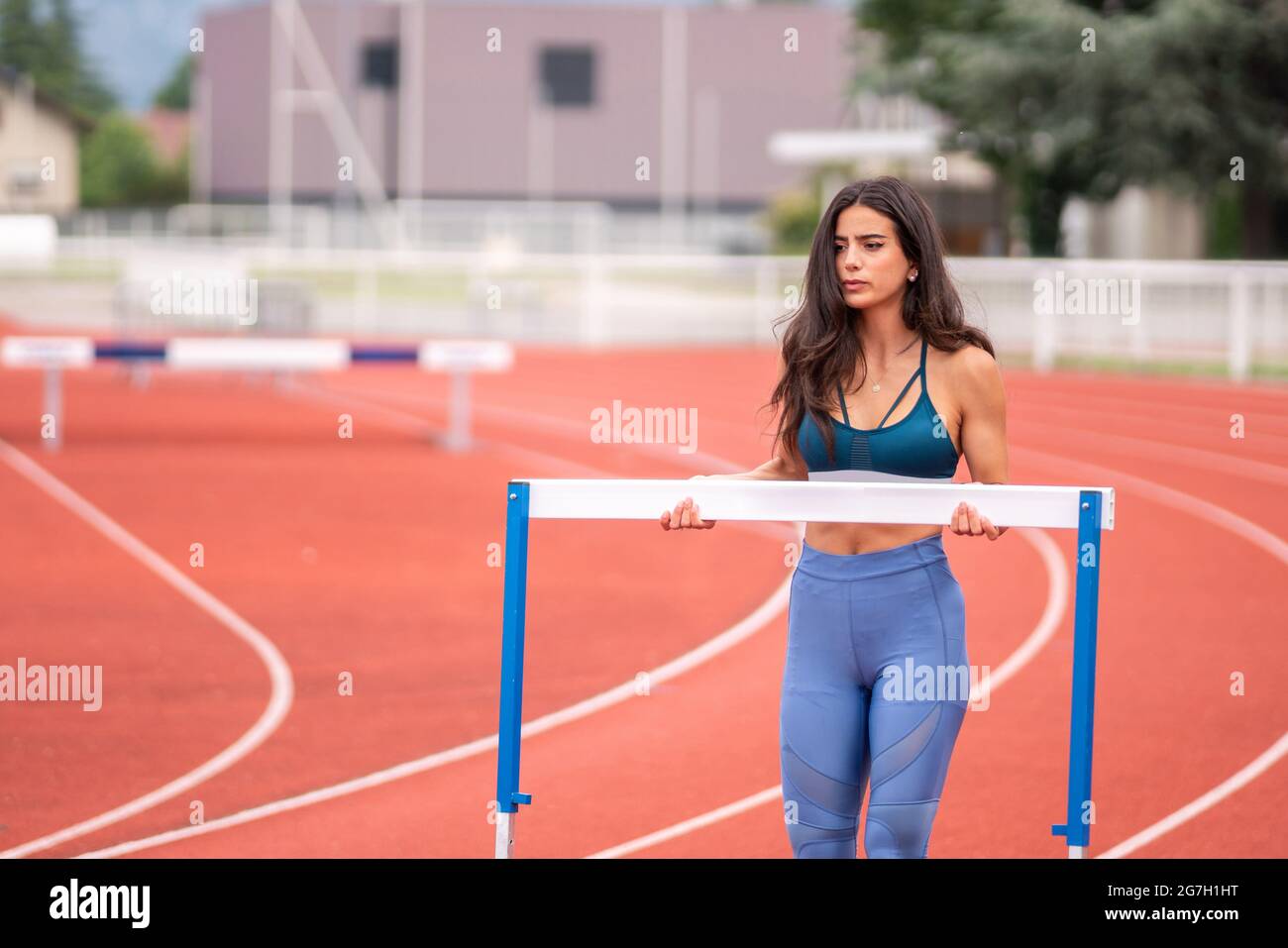 Giovane atleta ispanica che porta un ostacolo mentre si prepara per correre con ostacoli in pista dello stadio sportivo Foto Stock