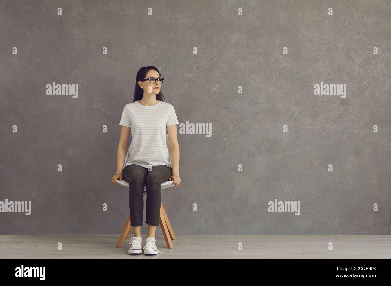Una giovane bella ragazza si siede su uno sgabello bianco in piena crescita, in una T-shirt, scarpe sportive. Foto Stock