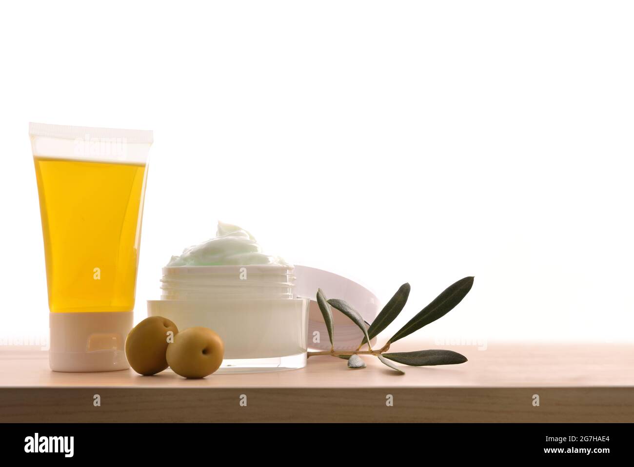 Olio e crema cosmetica idratante con estratto di oliva per la pelle con rametto e olive su tavola di legno. Vista frontale. Foto Stock