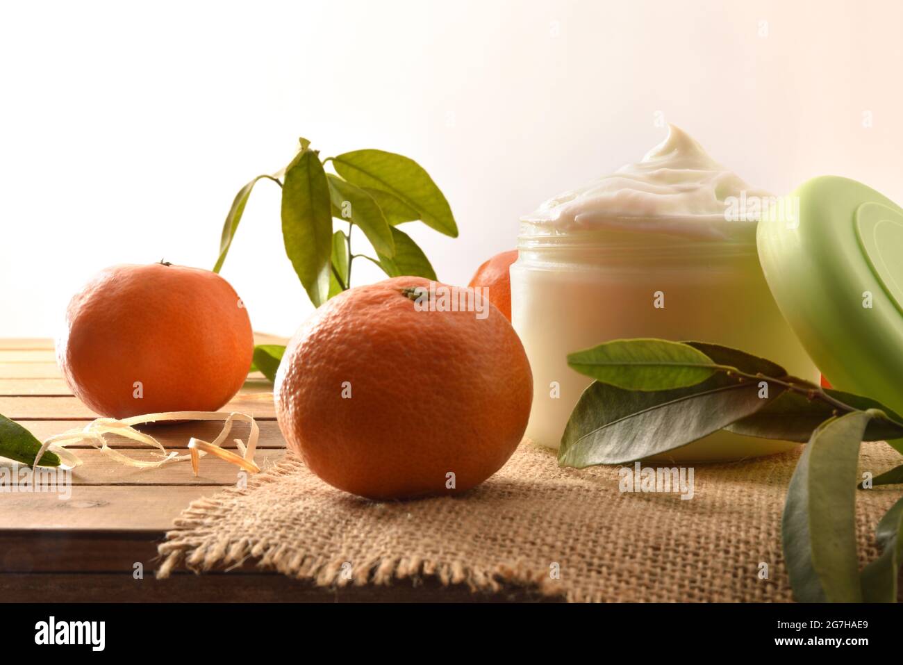 Crema naturale di pelle con estratto di mandarino con frutta e foglie su tavola di legno. Vista frontale. Foto Stock