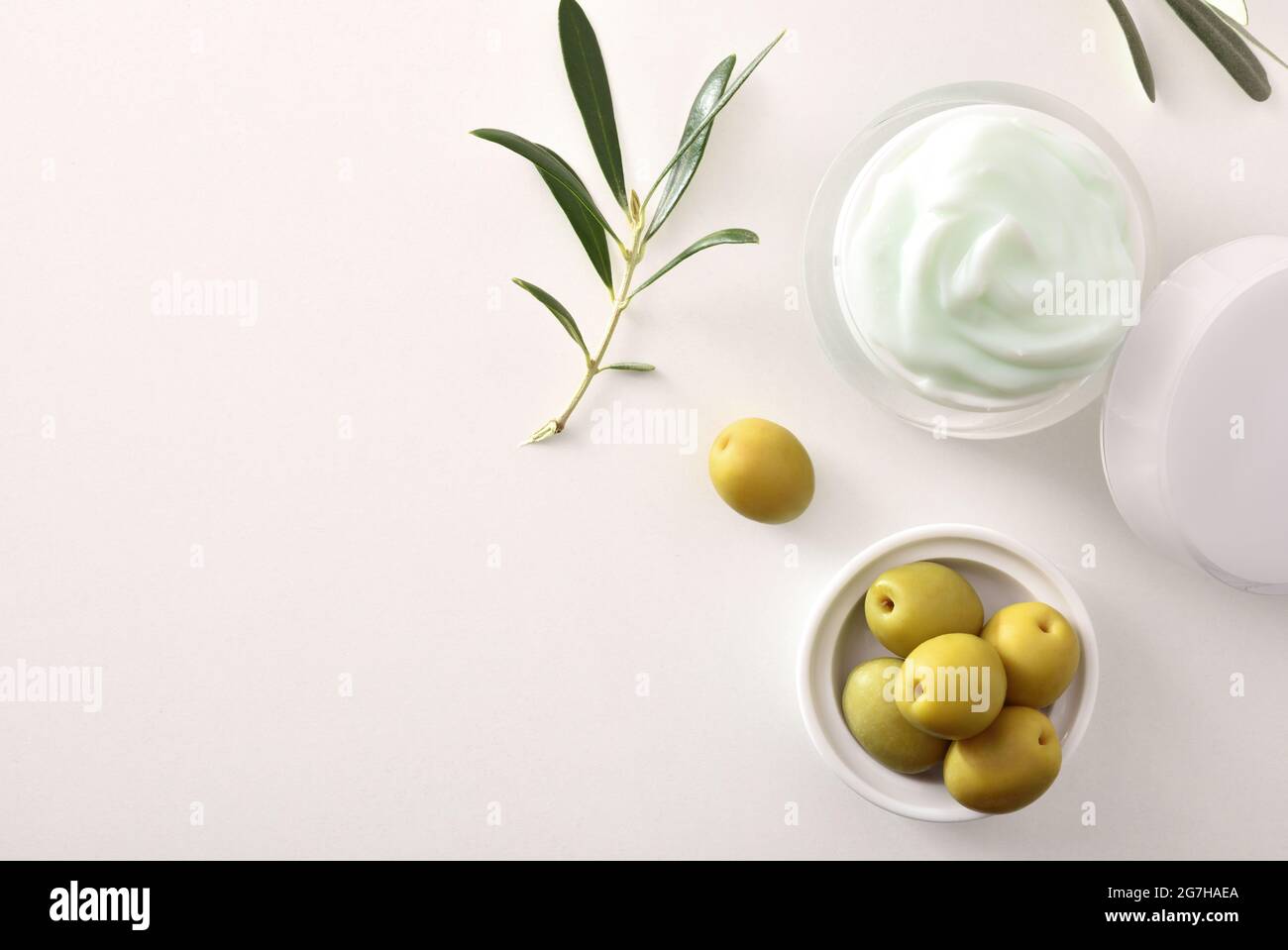 Crema cosmetica idratante con estratto di oliva per la pelle con rametto e olive su tavola bianca. Vista dall'alto. Foto Stock