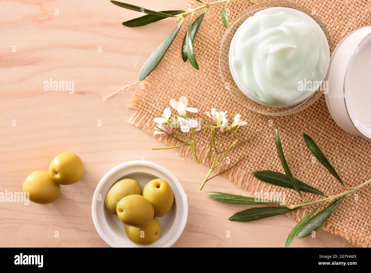 Crema cosmetica idratante con estratto di oliva per la pelle con rametto e olive su tavola di legno. Vista dall'alto. Foto Stock
