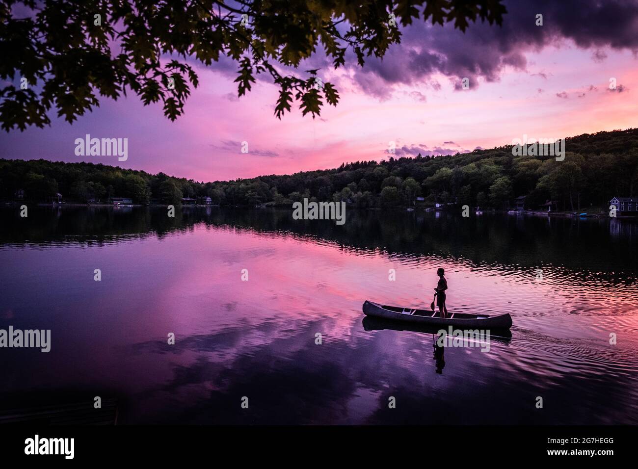 Il canoista si alza in canoa mentre si addica su un piccolo lago vicino a Cooperstown, NY, al tramonto. Foto Stock