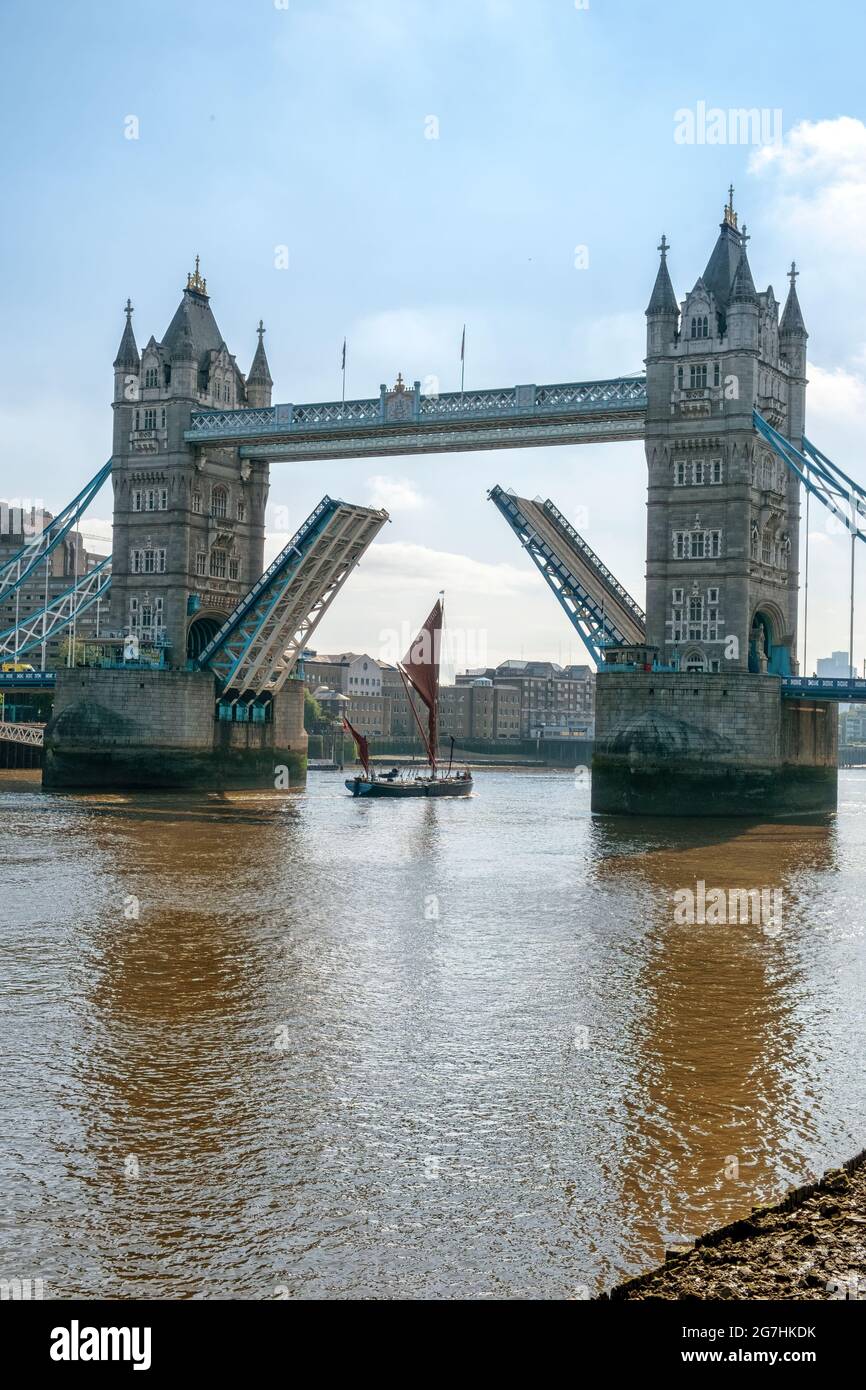 Chiatta da vela del Tamigi Ardwina passando sotto il Tower Bridge che attraversa il Tamigi con la strada sollevata per facilitare la sua navigazione in una mattina di inizio estate Foto Stock