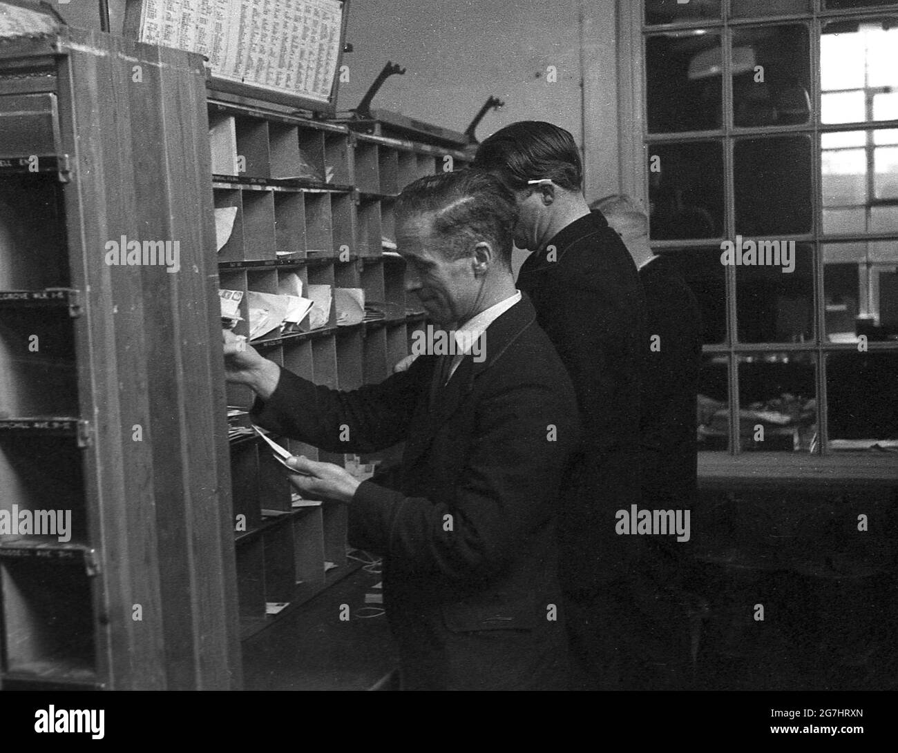 Anni '50, storici, tre uomini GPO lavoratori smistare le lettere o la posta nel cubby o pigeon-buchi su una mensola diviso in il distretto dfferent strade, Londra, Inghilterra, Regno Unito. Foto Stock